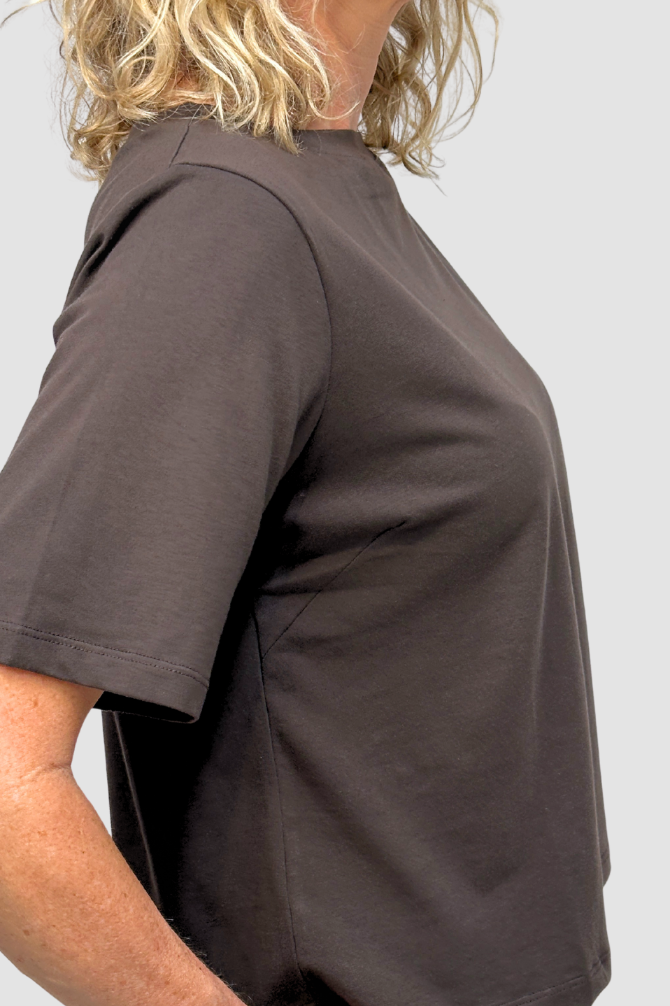Side view of a woman in a plain brown short-sleeve ethical cotton t-shirt against a light background