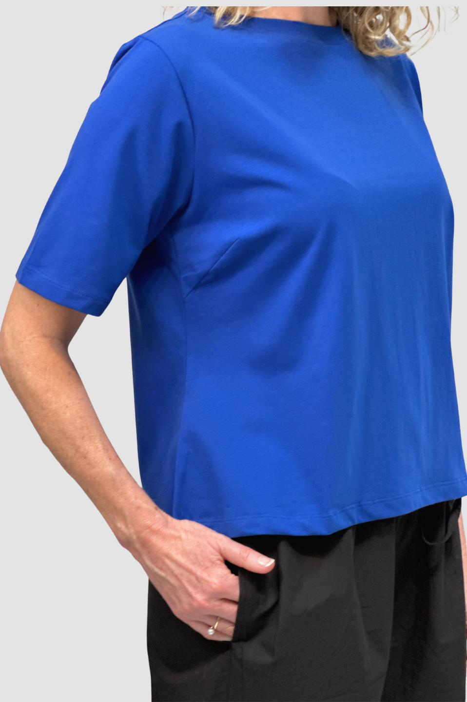Woman wearing a royal blue short-sleeve cotton top with black pants against a light gray background