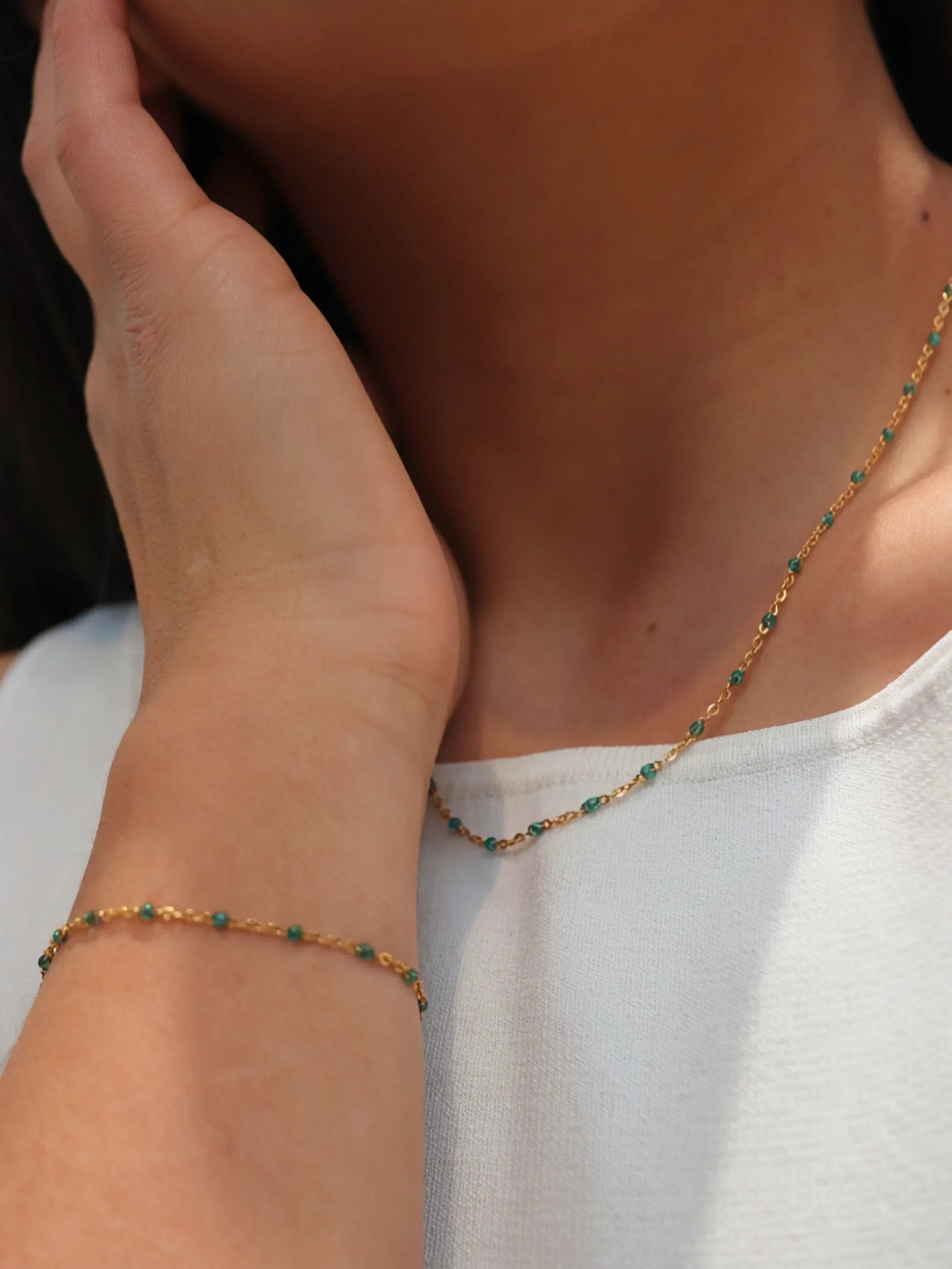 Close-up of a person wearing a delicate gold necklace with green beads.