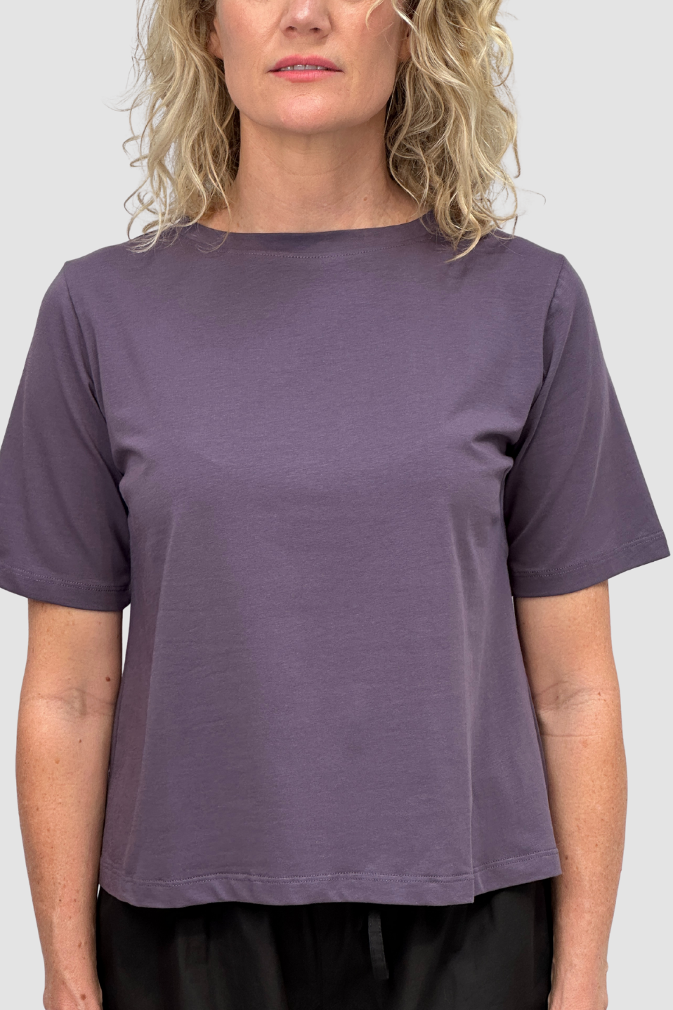 Woman wearing a plain purple short-sleeve t-shirt with a round neckline against a neutral background