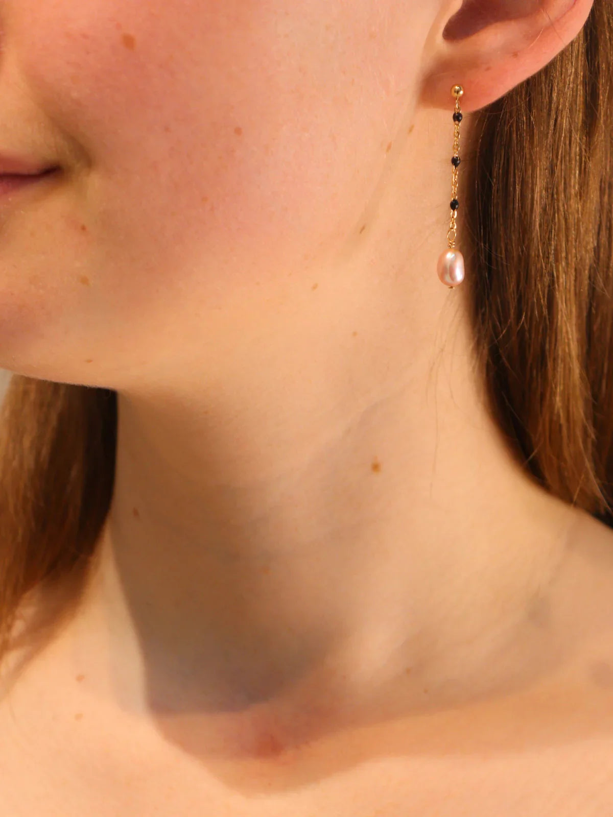 Gold chain link drop earring with pearl pendant, worn on ear.