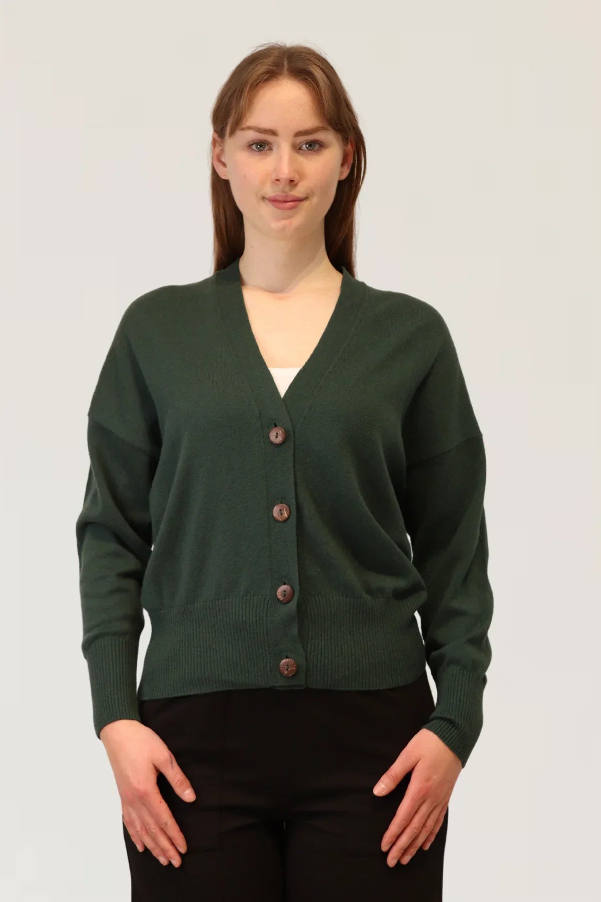 Woman wearing a green cardigan with brown buttons on a white background