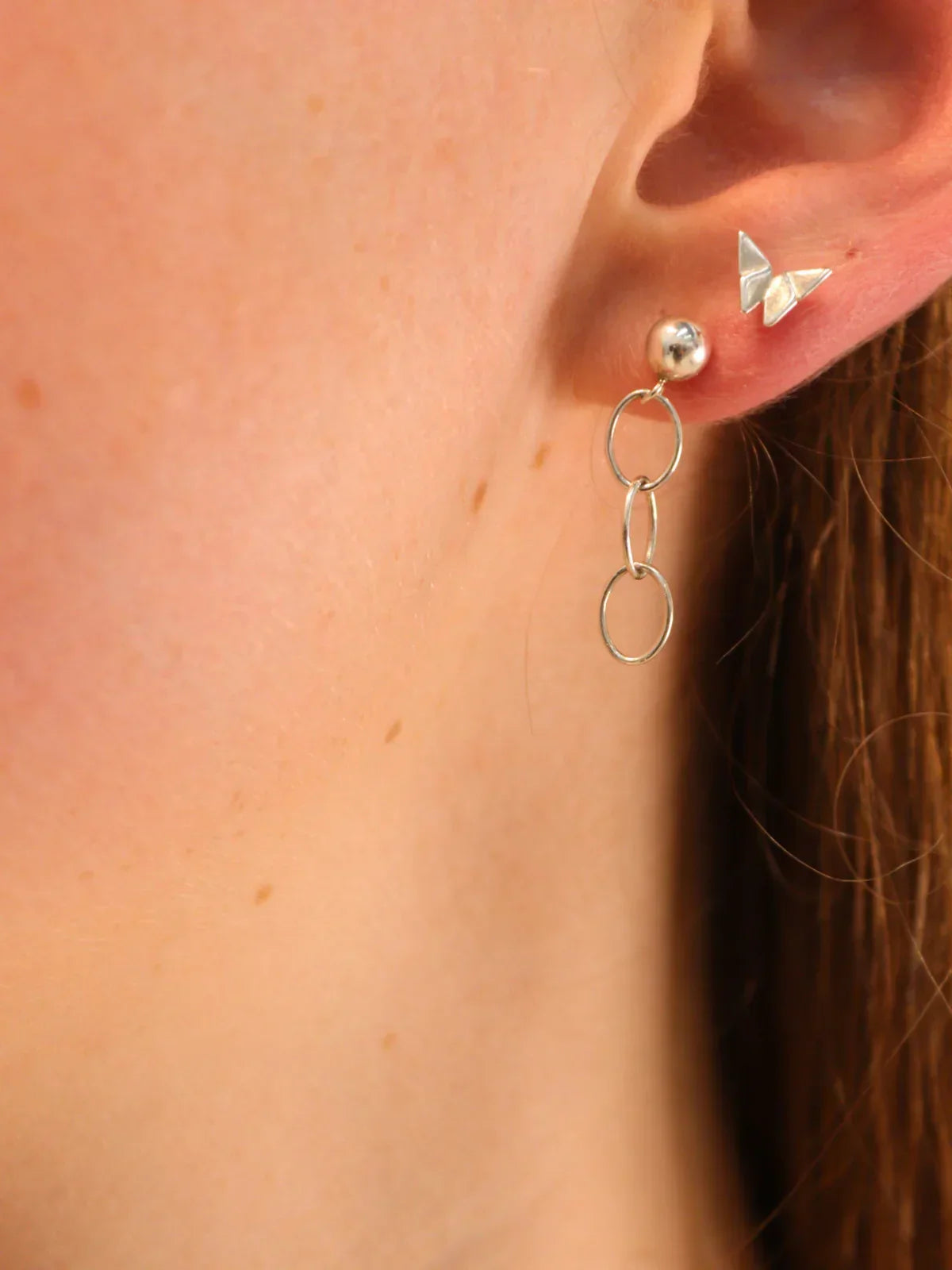 Close-up of sterling silver dangle earrings with double hoop design, paired with a small butterfly stud, worn on ear.