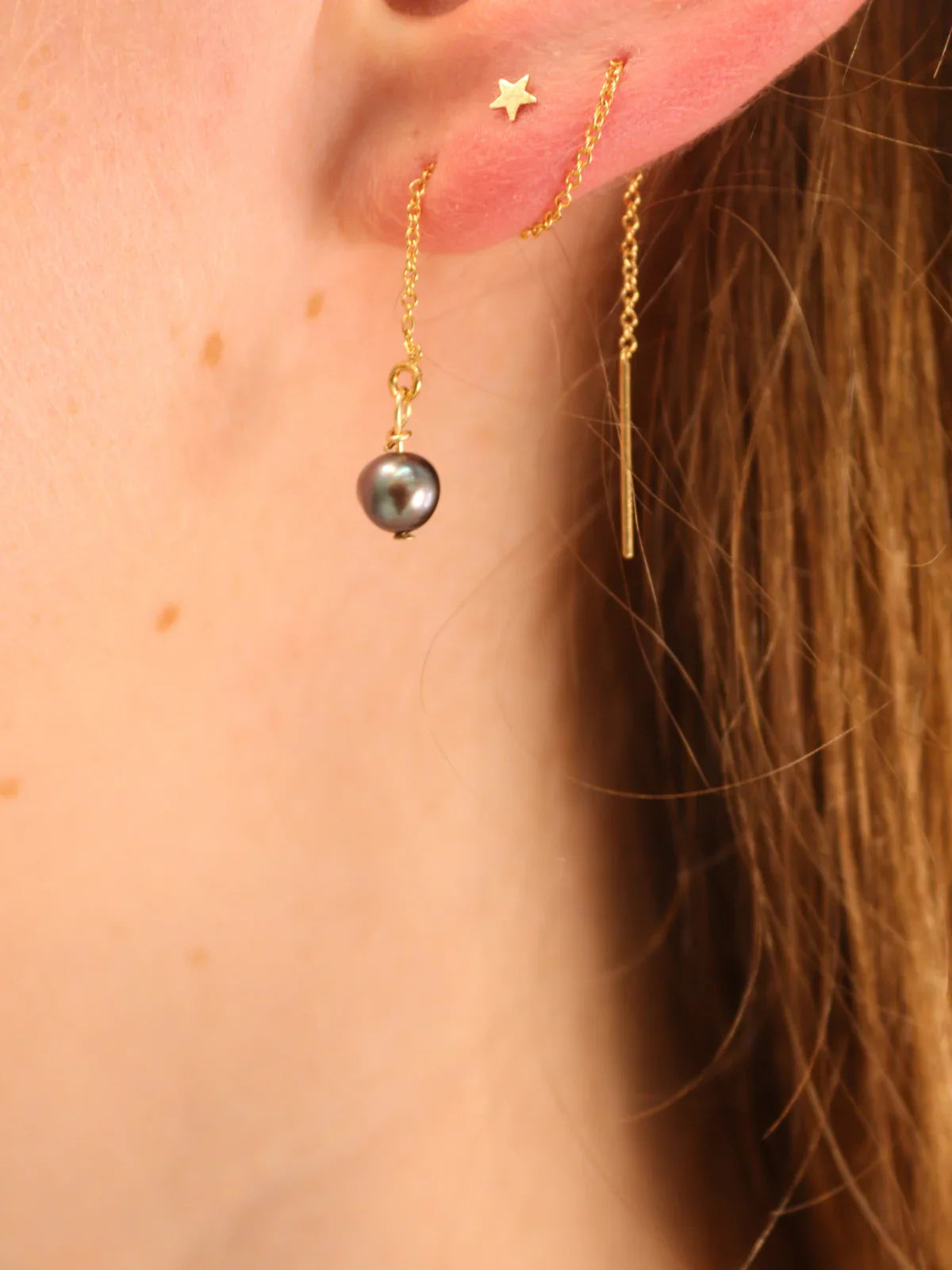 Woman wearing gold black pearl threader earrings with matching star stud.