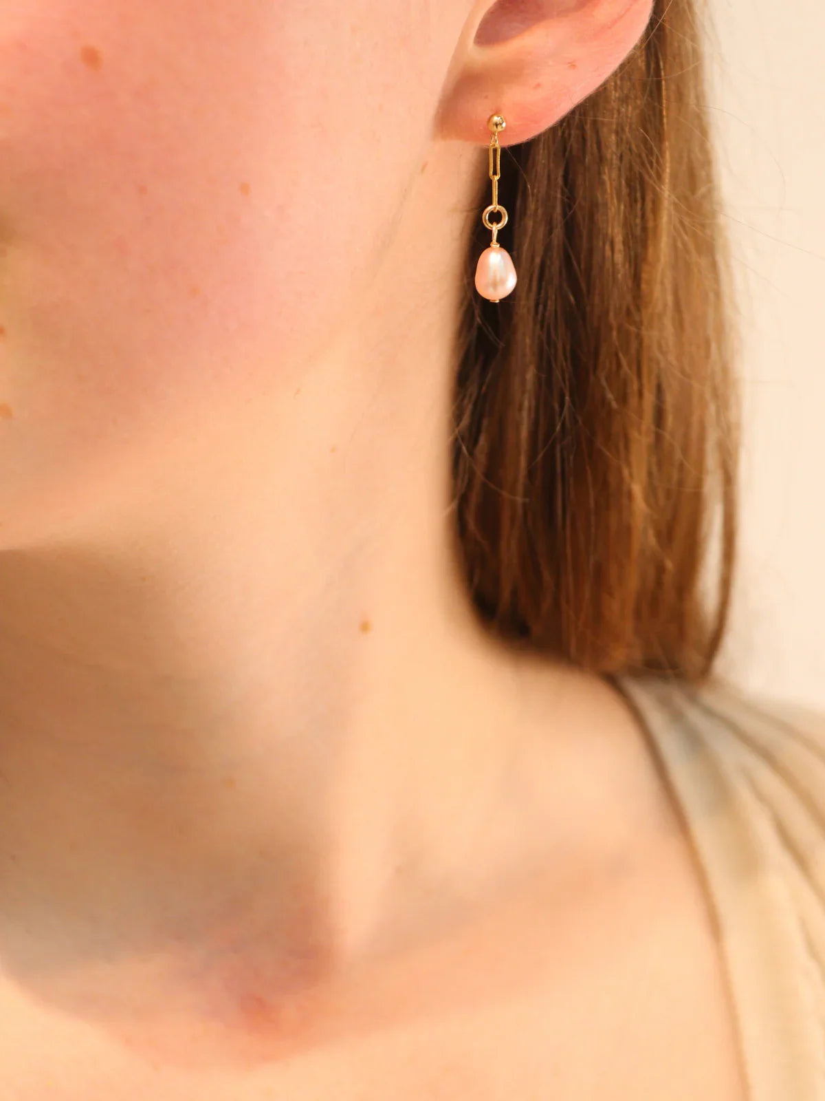 Gold link drop earring with teardrop white pearl pendant, worn on ear.