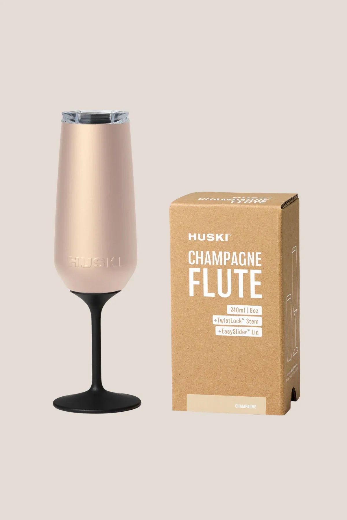 Rose gold champagne flute with black base next to its packaging box on a beige background