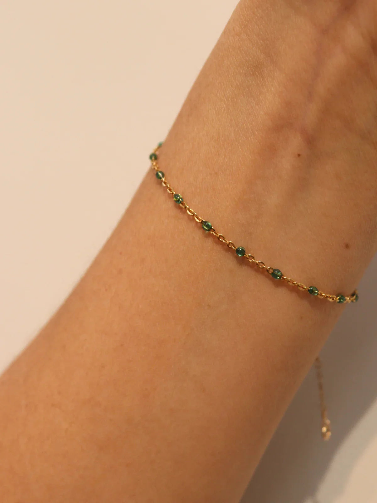 Gold anklet with green beads on a person's ankle against a beige background