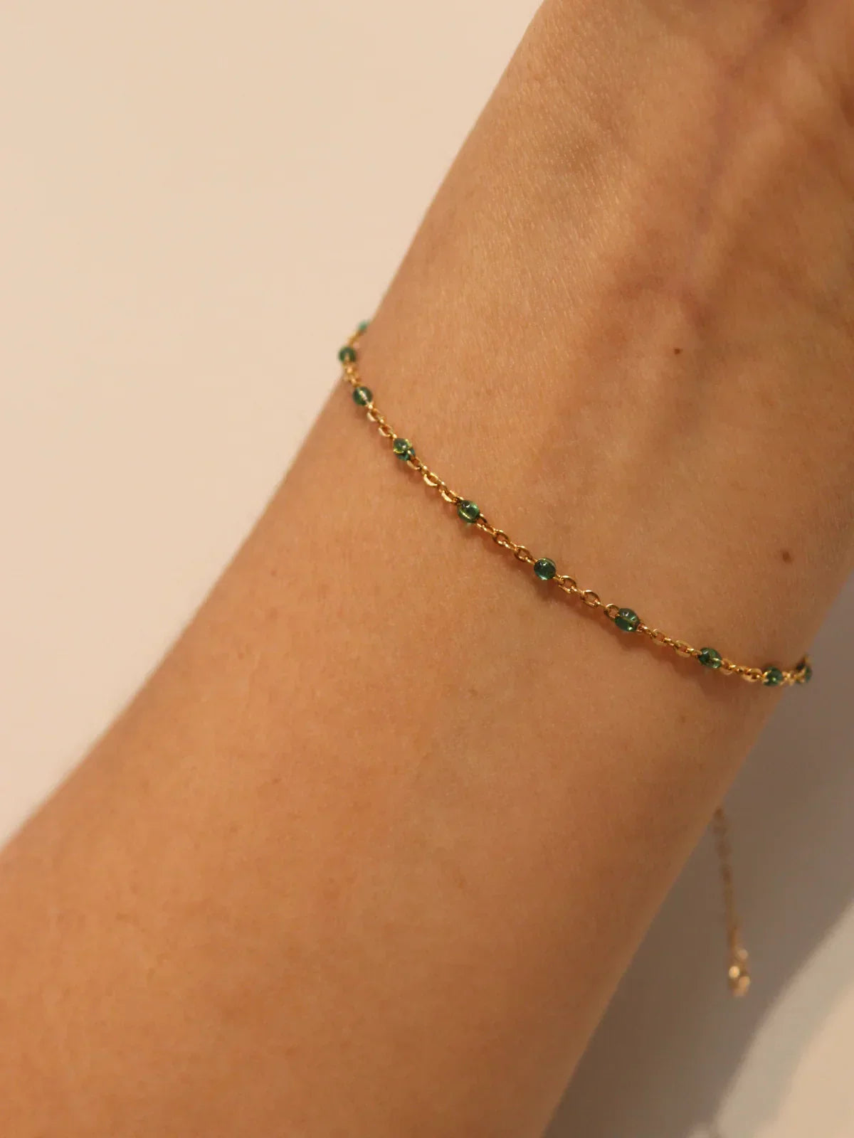 Gold anklet with green beads on a person's ankle against a beige background