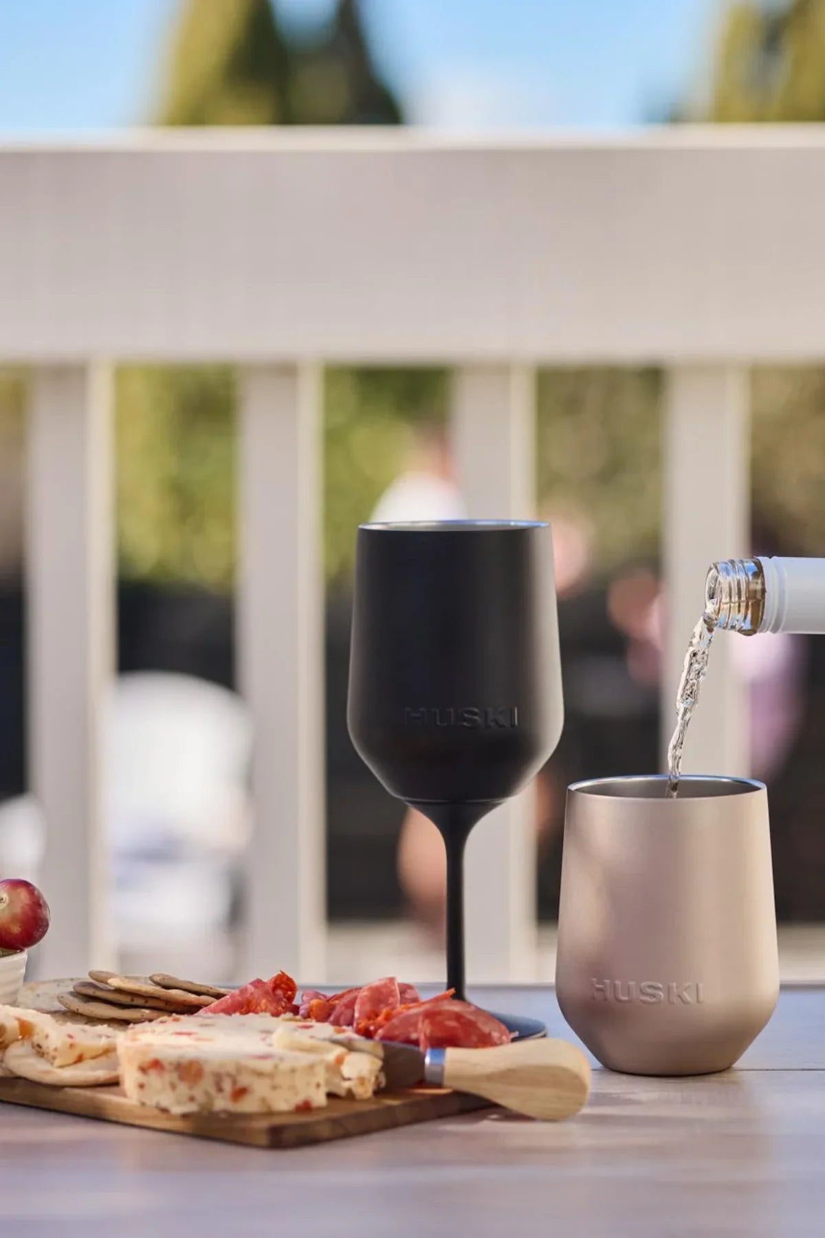 Two insulated cups, one black and one silver, being filled with a liquid on a table with food.