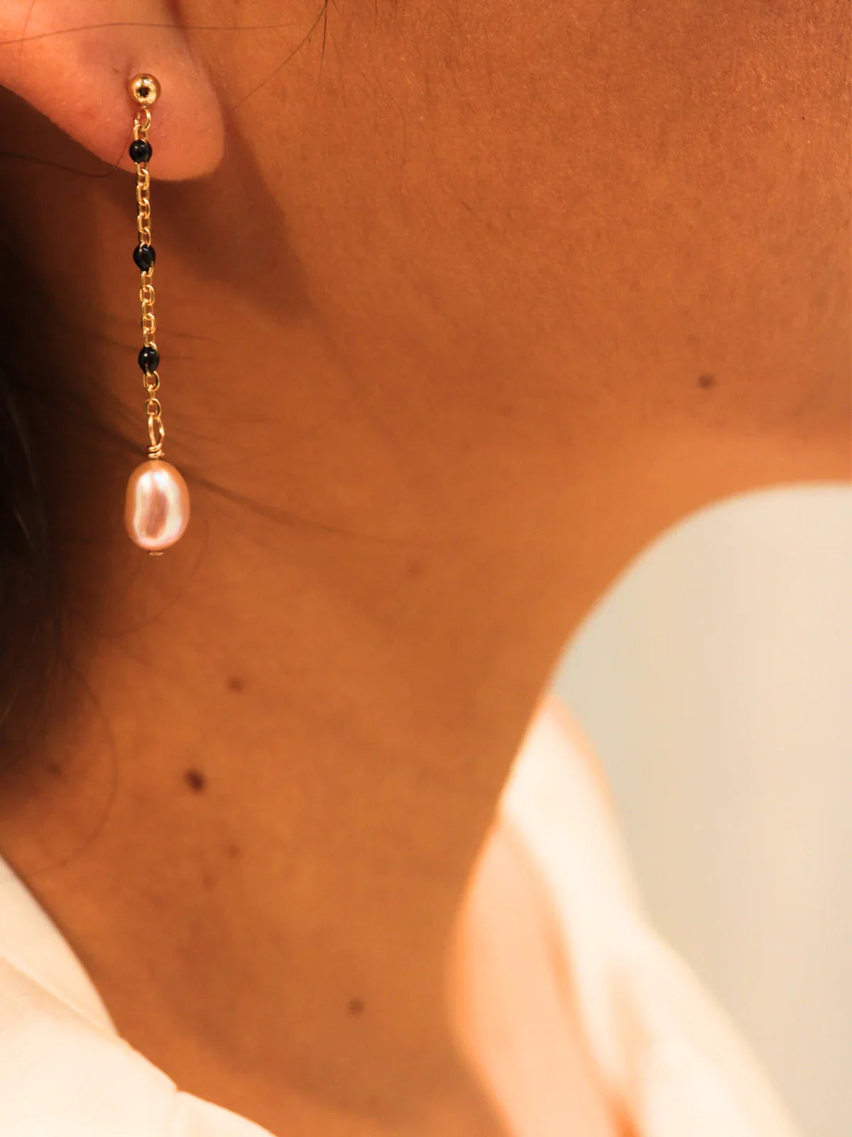 Gold chain link drop earring with oval pearl, shown on model’s ear.