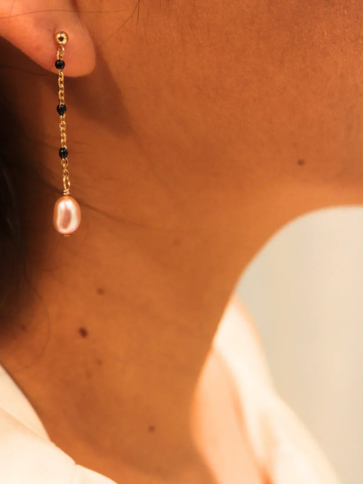 Gold chain link drop earring with oval pearl, shown on model’s ear.