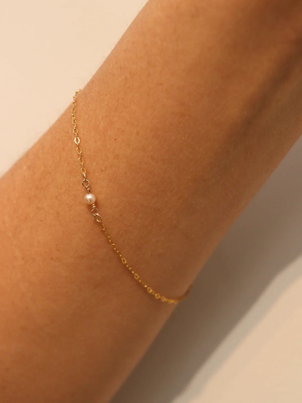 Gold bracelet with a pearl on a wrist against a neutral background