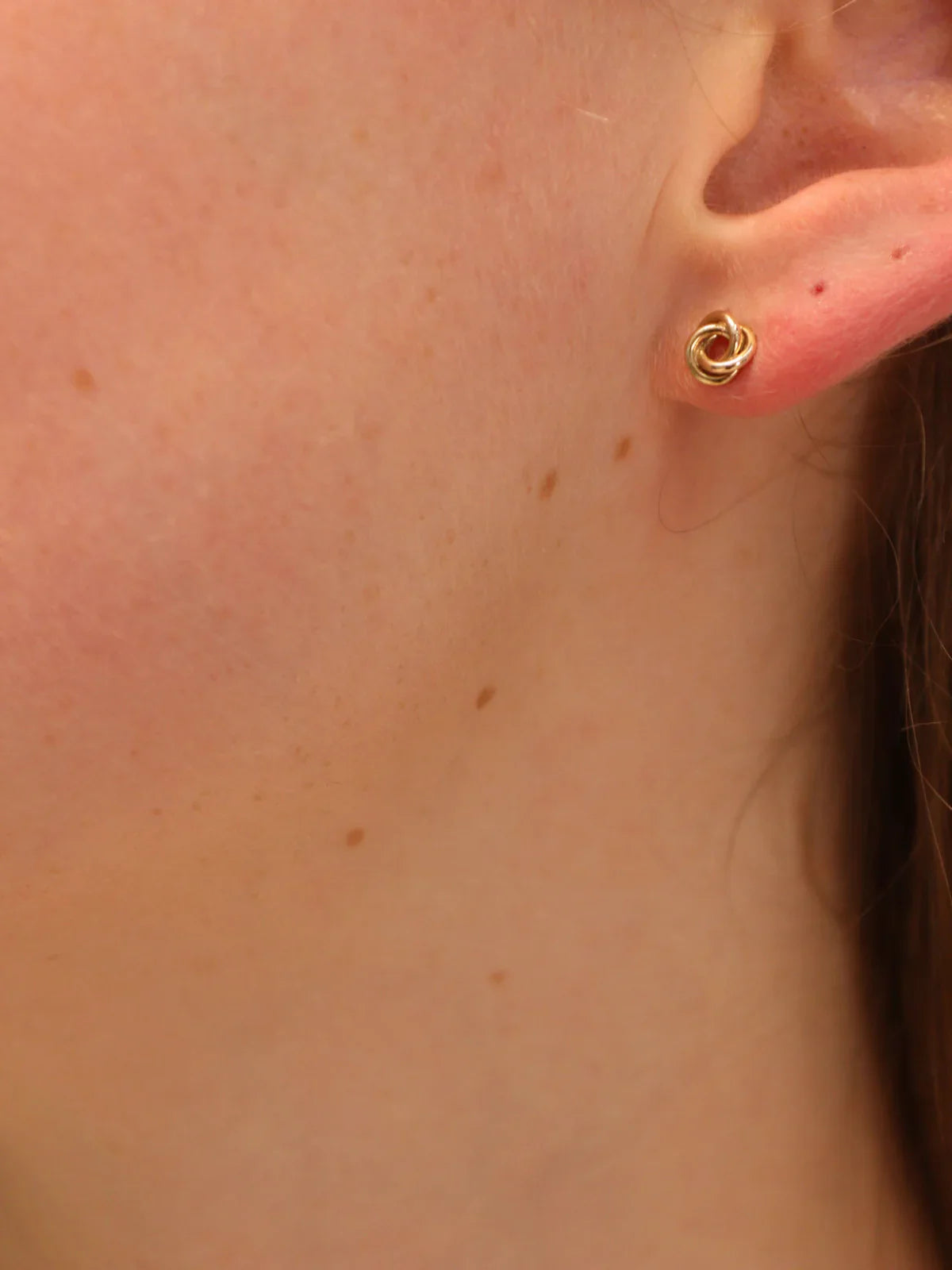 Gold knot stud earring, worn on ear.