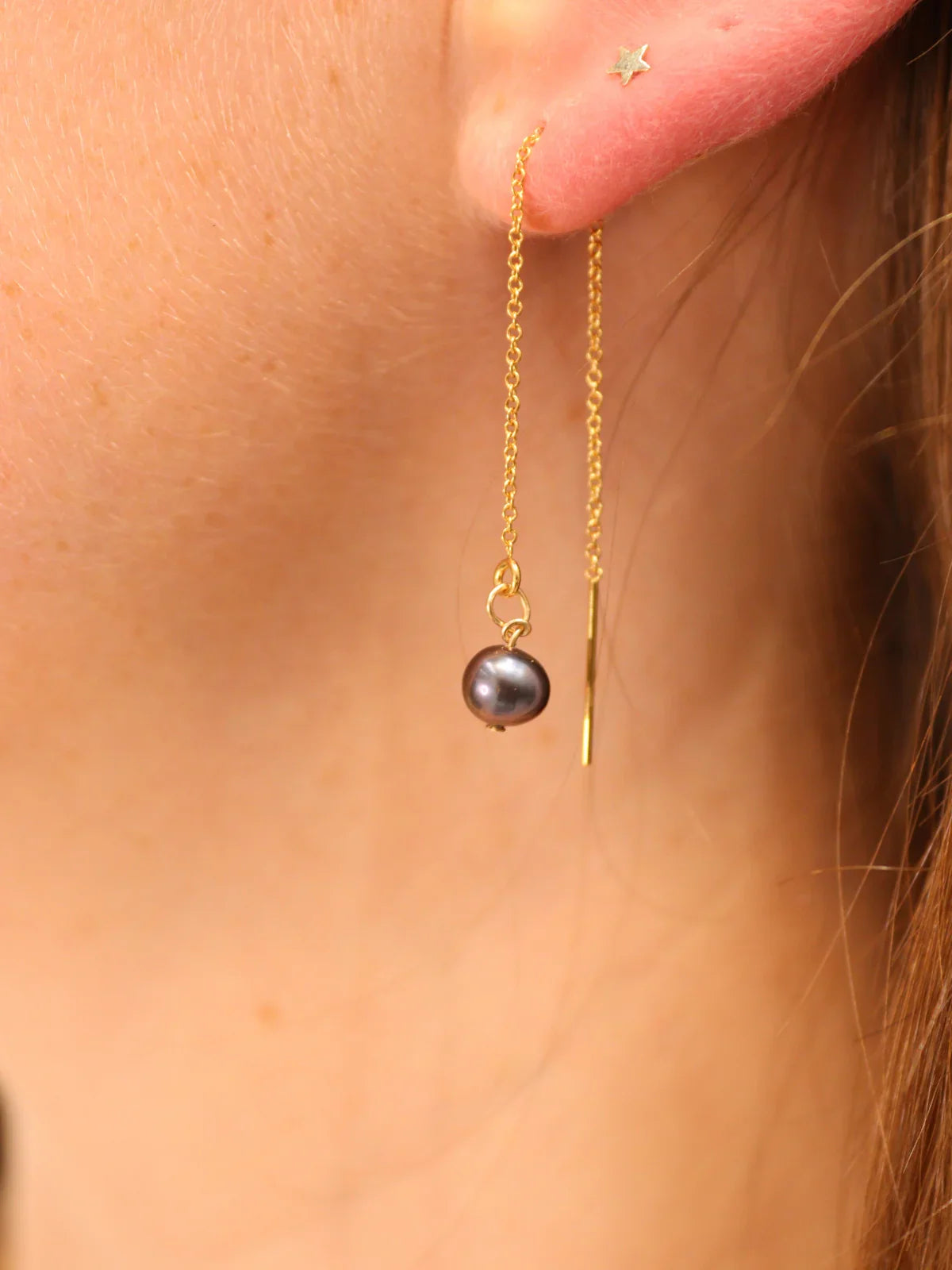 Black pearl drop threader earring on gold chain, shown on ear.