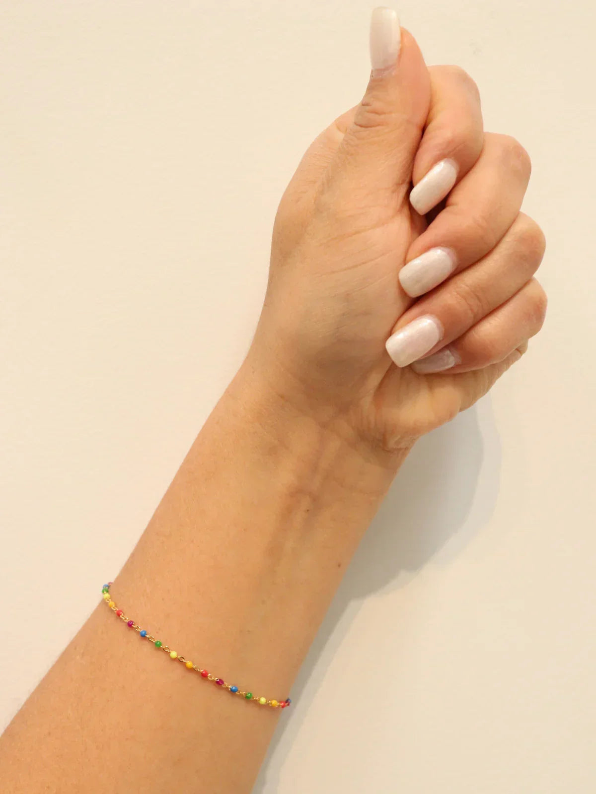 Hand wearing a colorful beaded bracelet on a plain background