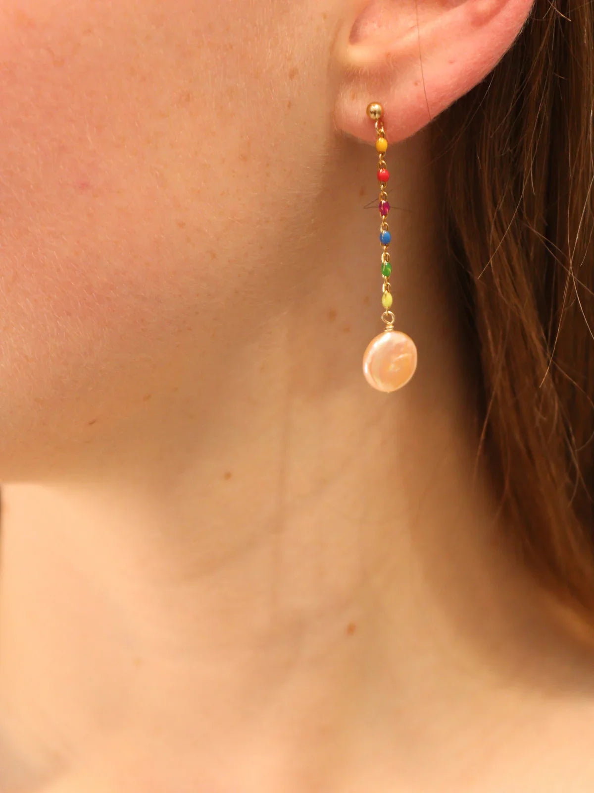 Gold drop earring with rainbow beaded chain and round pearl pendant, worn on ear.