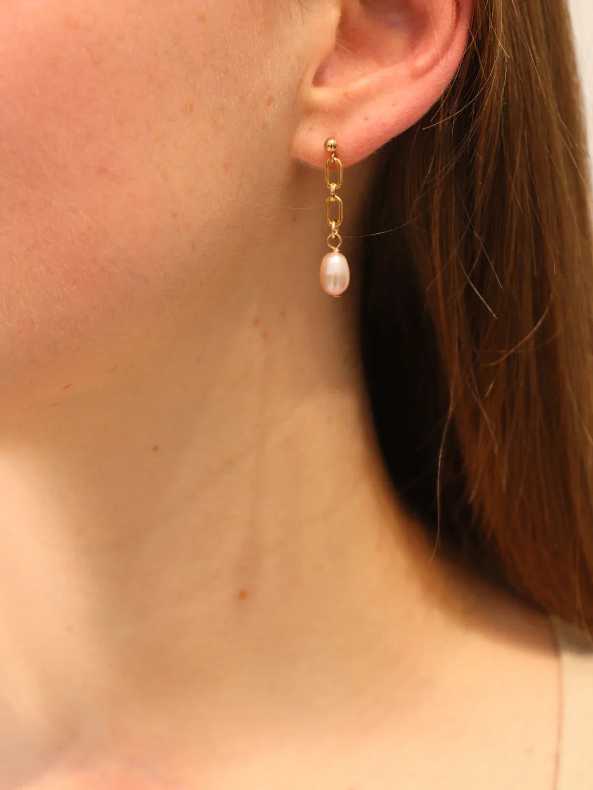 Gold chain link drop earring with a white pearl pendant, worn on ear.