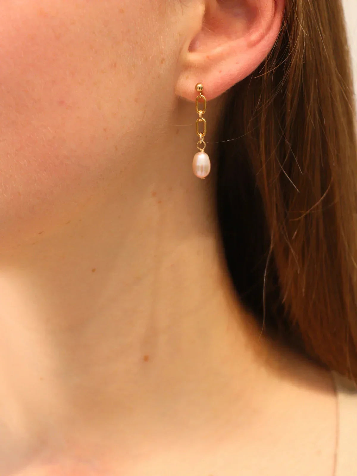 Gold chain link drop earring with a white pearl pendant, worn on ear.