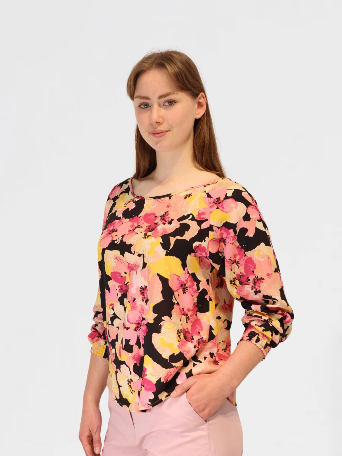 Woman wearing a floral print blouse with pink, yellow, and black pattern, paired with pink pants.