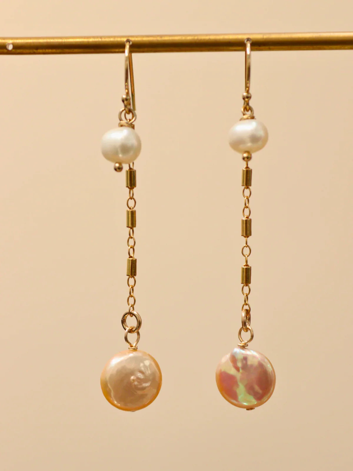 Pair of gold chain drop earrings featuring white pearl and flat coin pearl, displayed on jewellery stand.