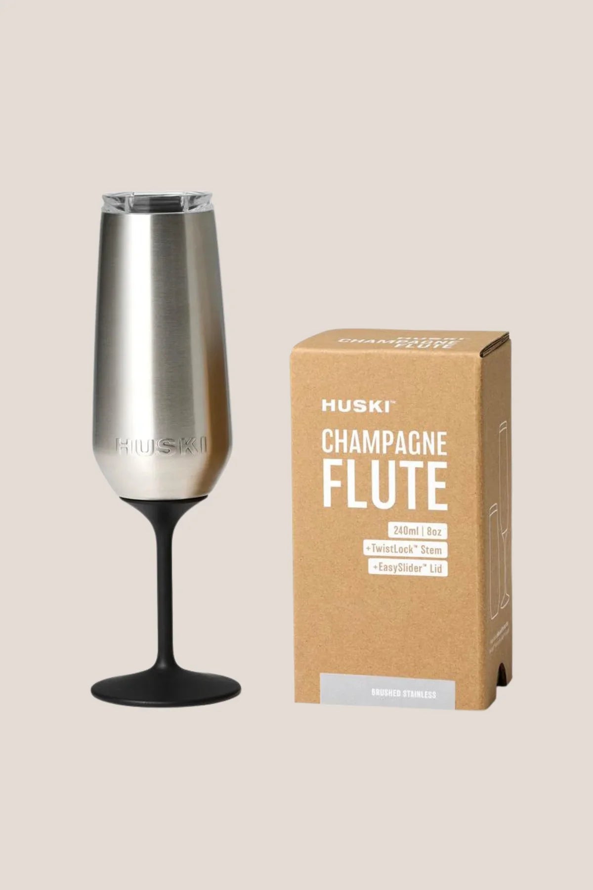 Silver champagne flute with black base next to its packaging box on a beige background