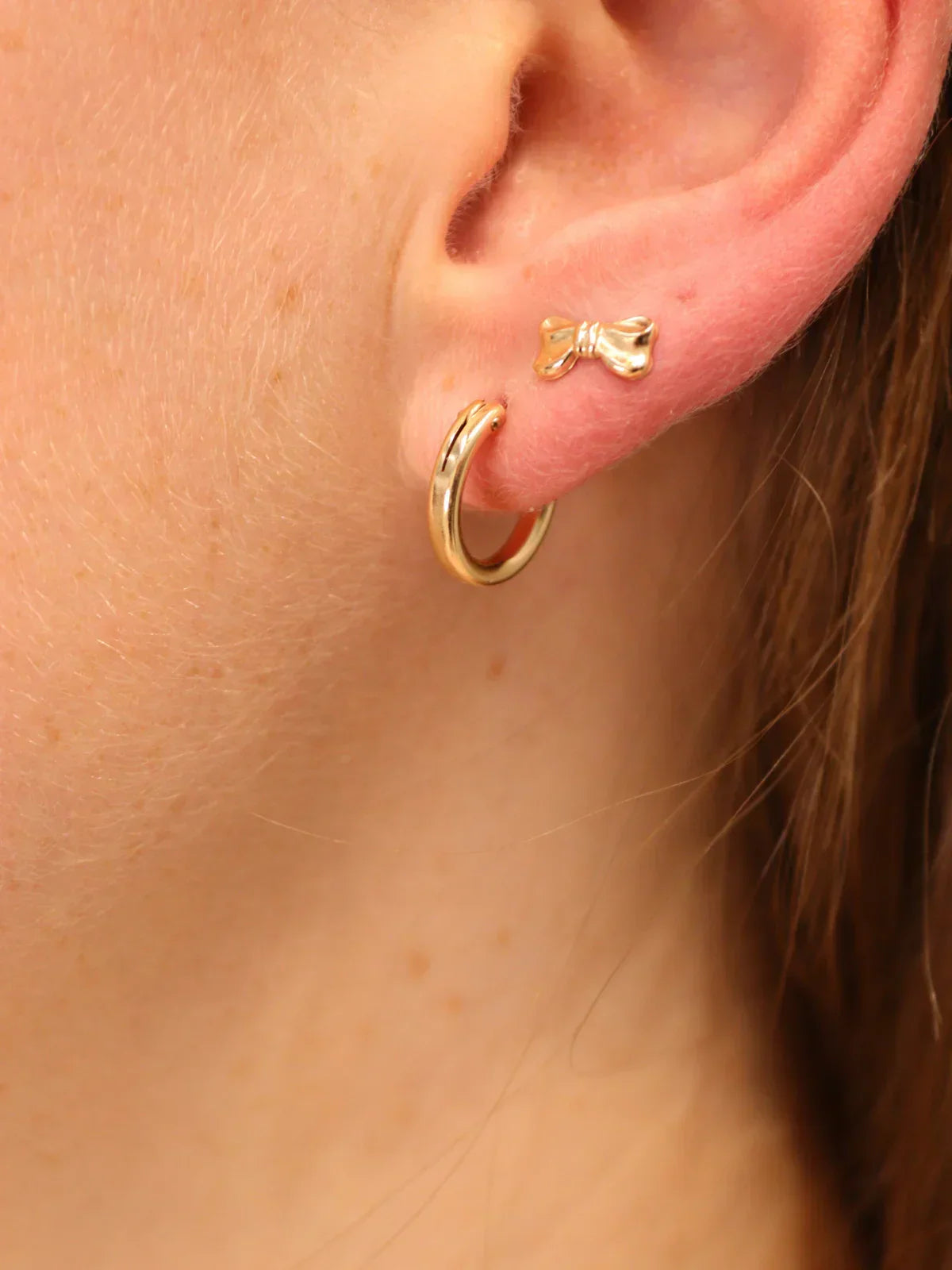Delicate gold hoop earring paired with a small gold bow stud.