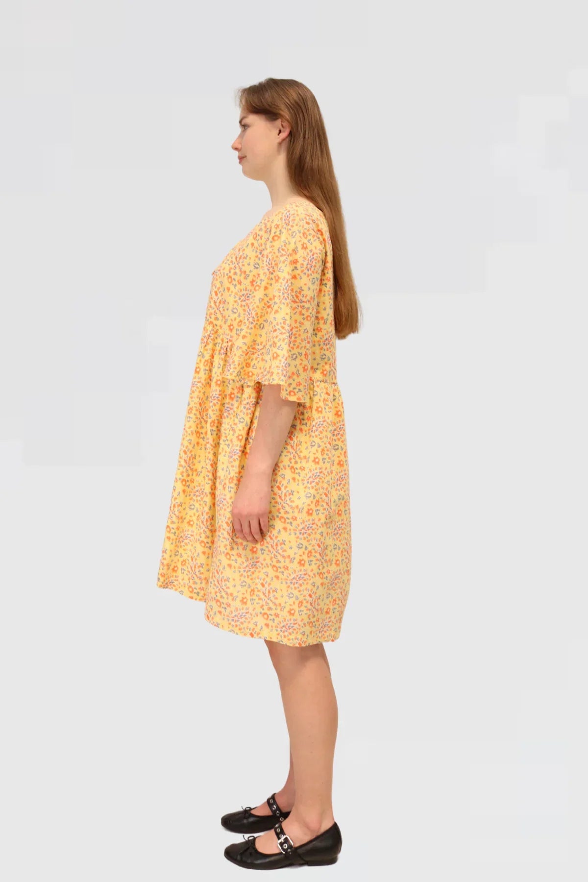 Woman wearing a yellow floral dress , Made ethically from 100% natural cotton on a plain background