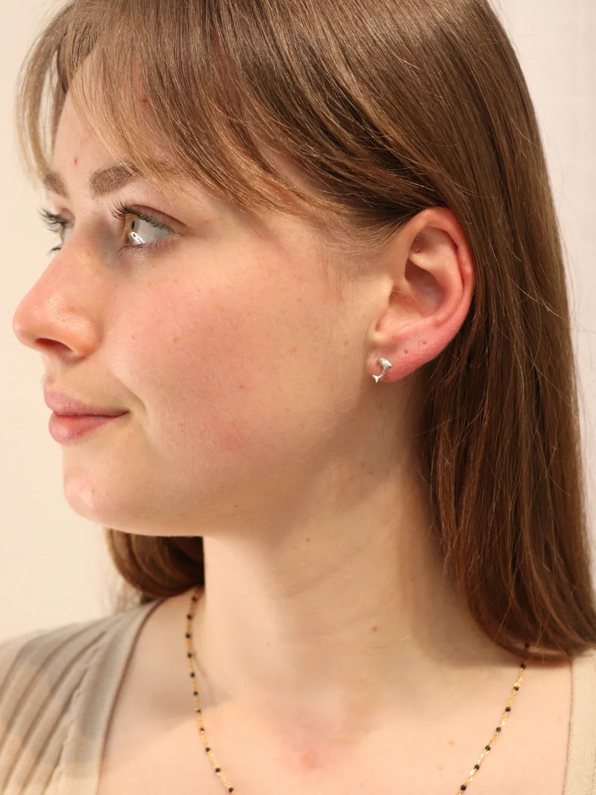 Close-up of silver dolphin stud earring on ear.