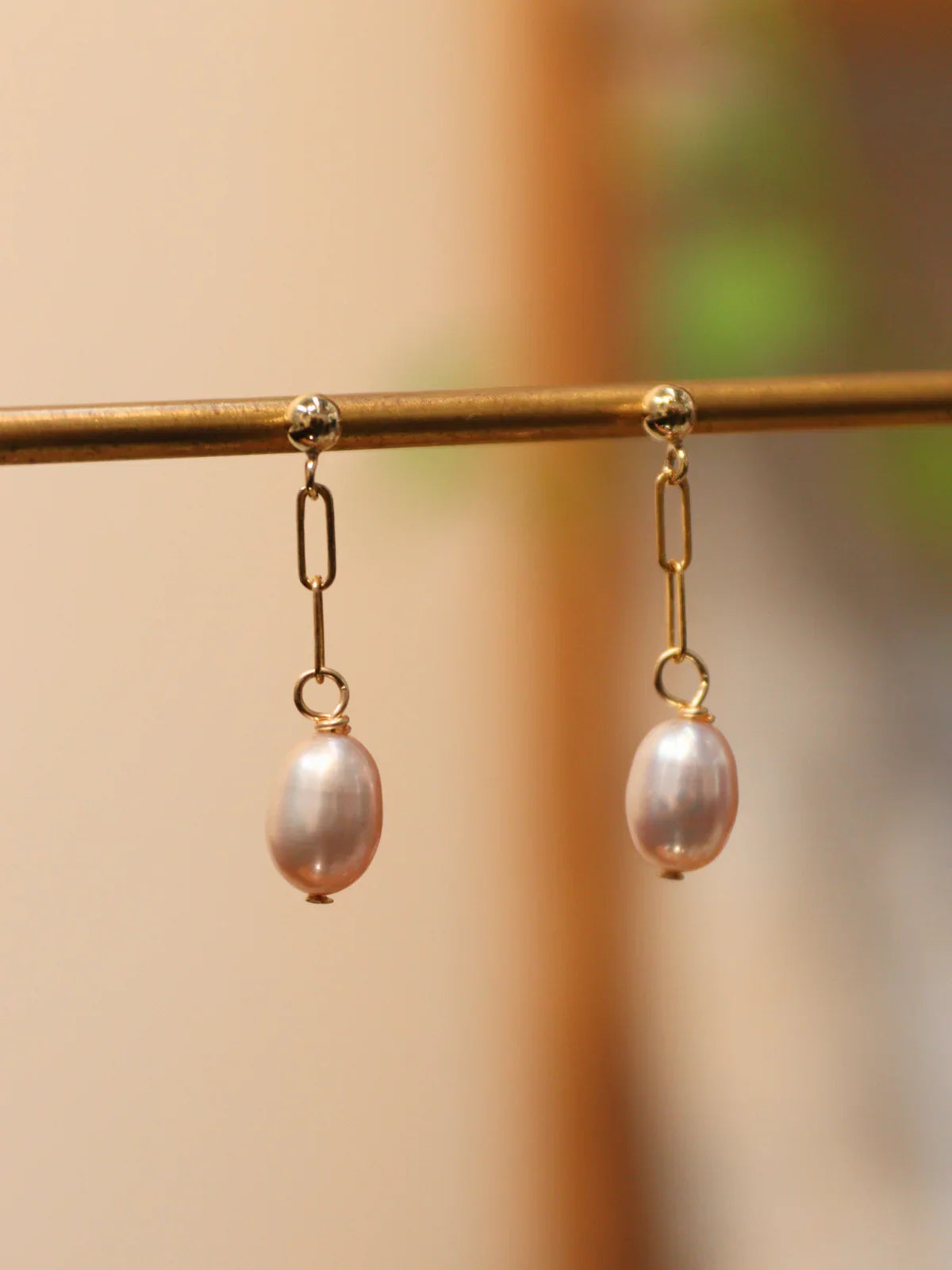 Pair of gold link drop earrings with oval white pearls, displayed on a jewelry stand.