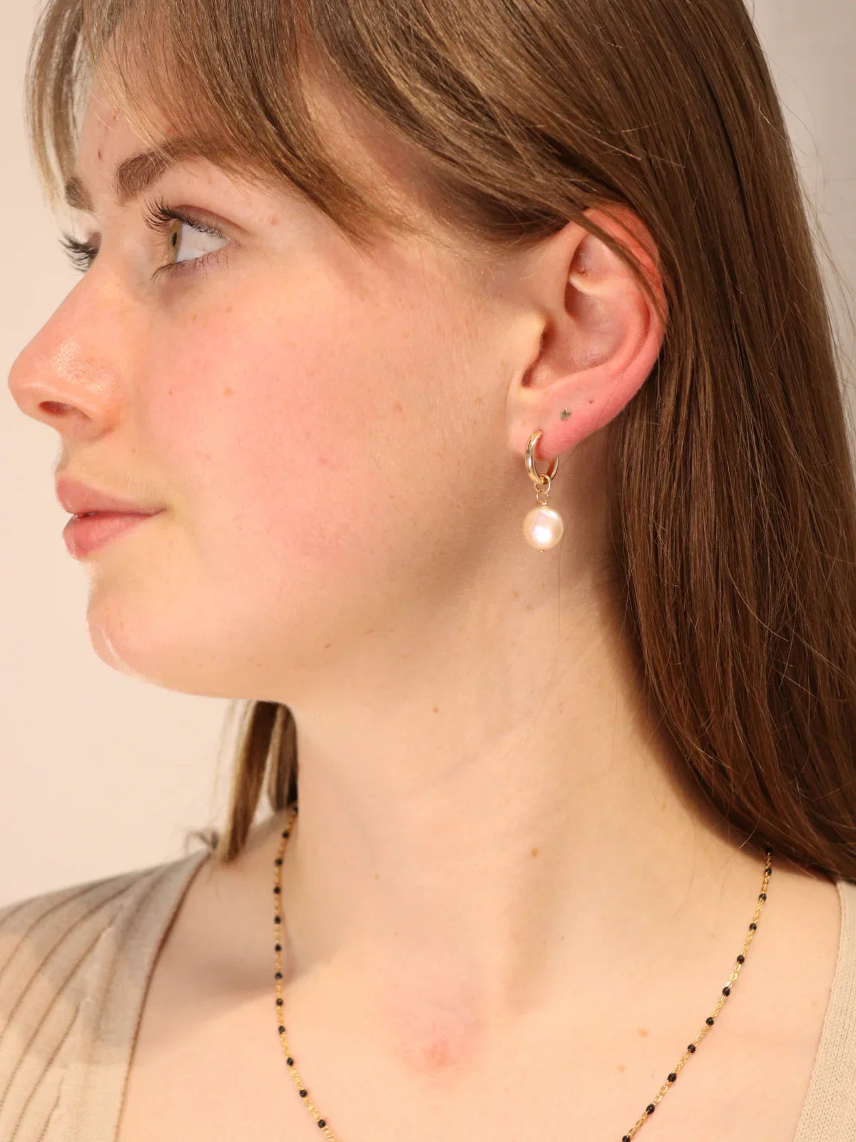 Woman wearing gold hoop earrings with dangling coin pearls.