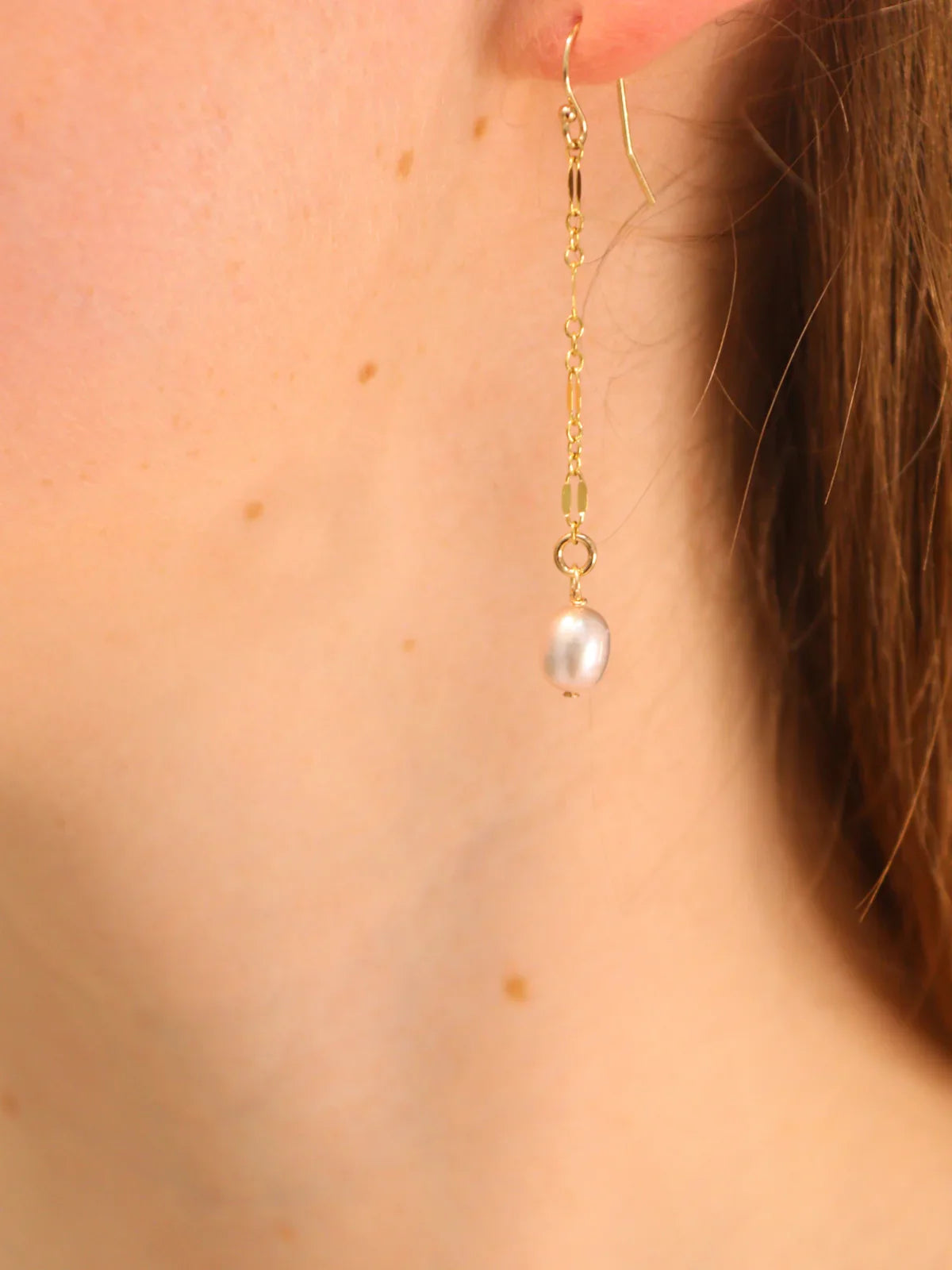 Woman wearing long gold chain drop earring with a white pearl pendant.
