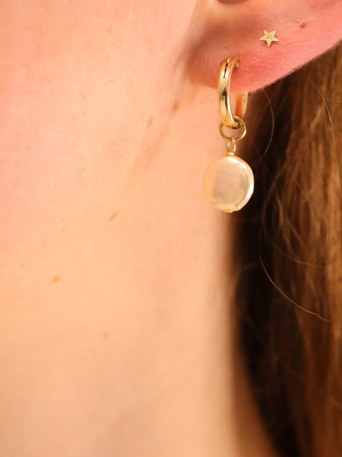 Delicate gold hoop with single coin pearl charm, shown on ear.