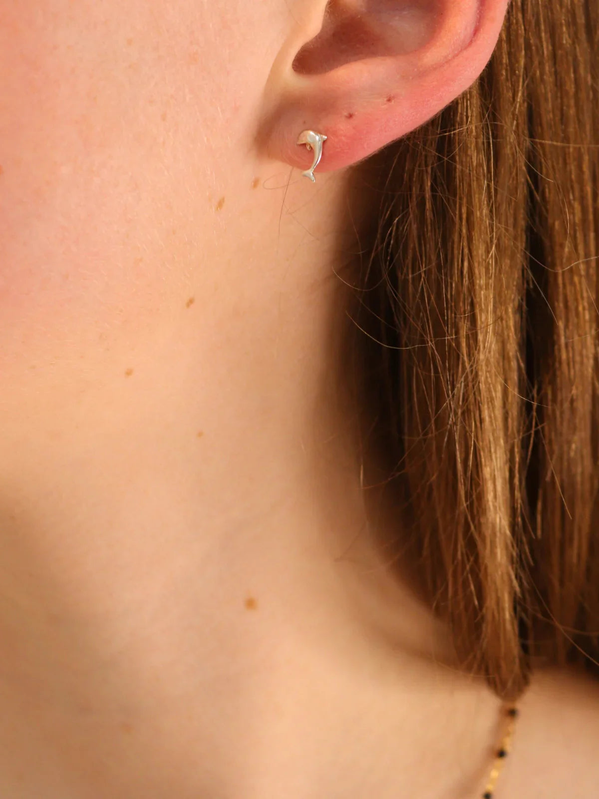 Silver dolphin stud earring, worn on ear.