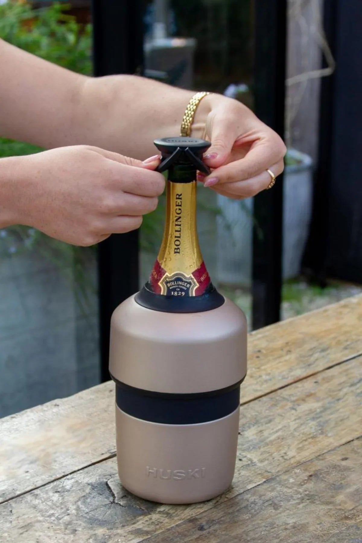 Person opening a Bollinger champagne bottle with a RUSK bottle opener on a wooden surface.