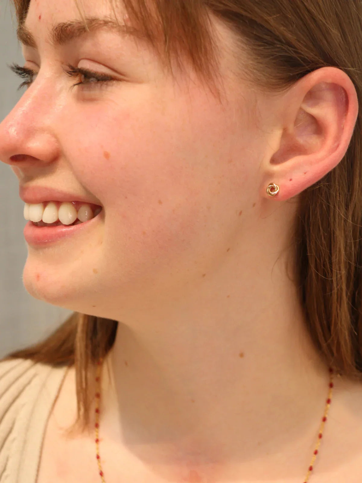 Woman wearing gold knot stud earrings with a delicate necklace.