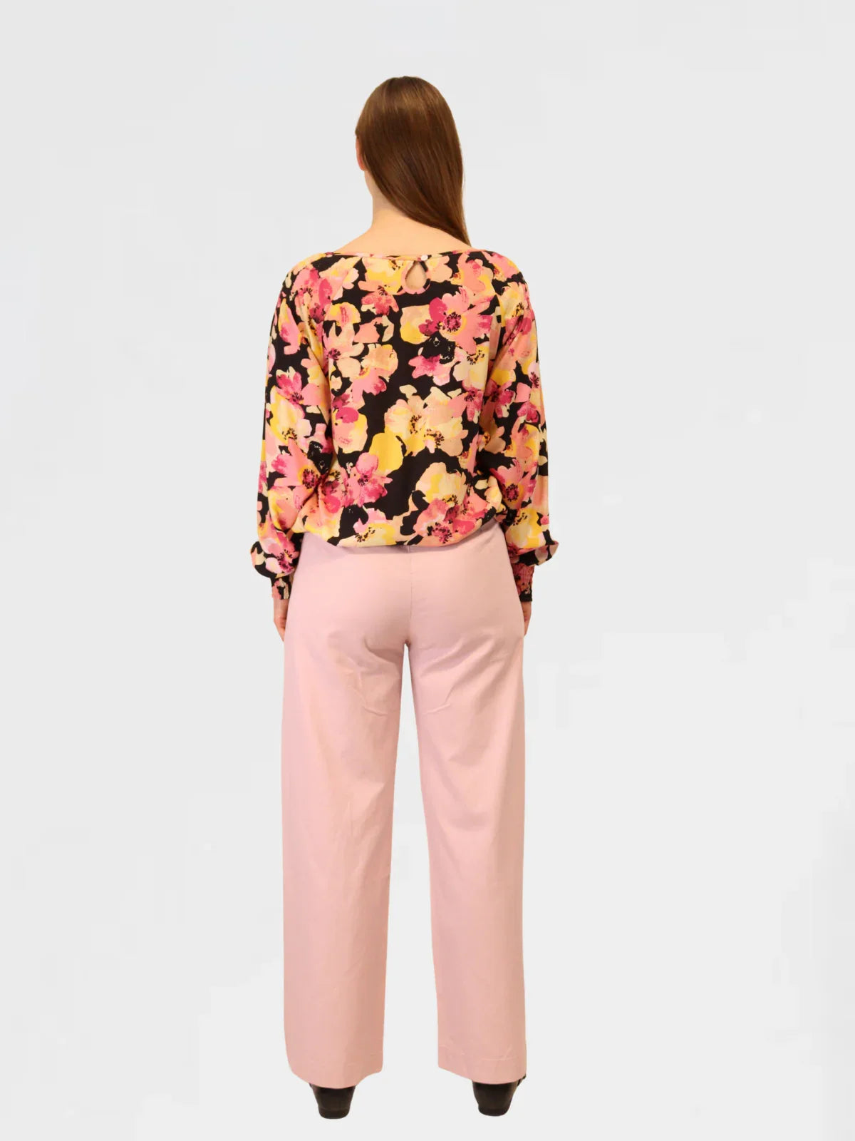 Woman wearing a floral blouse and pink pants on a white background