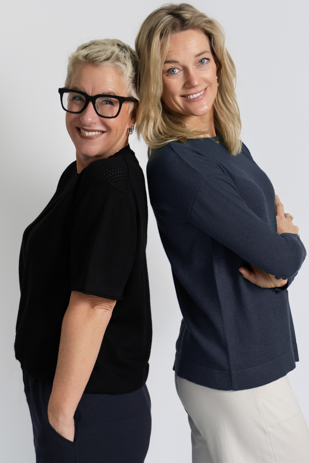 Two women standing back-to-back; one wearing the Cosmic Blue Silk Cashmere Knit with cream trousers