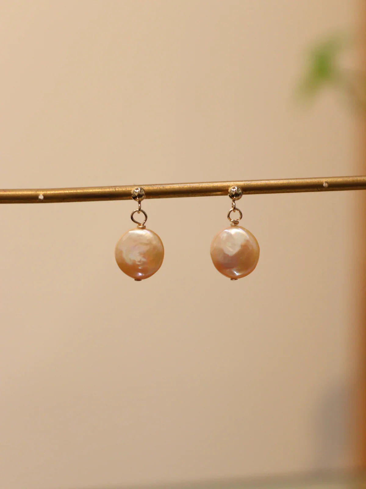 Pair of gold drop earrings featuring round white pearls, displayed on jewellery stand.