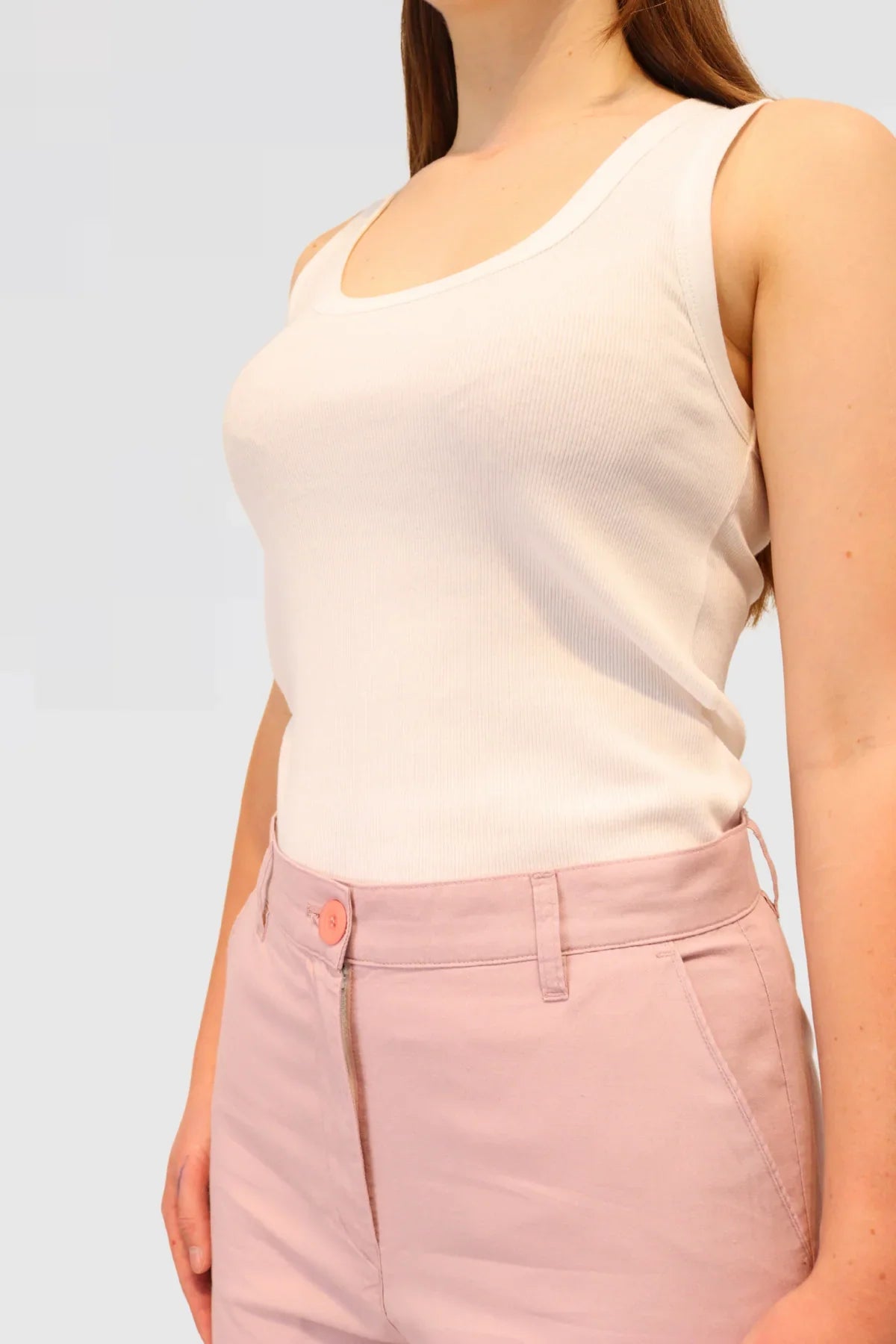 Person wearing a white tank top and pink pants against a light grey background