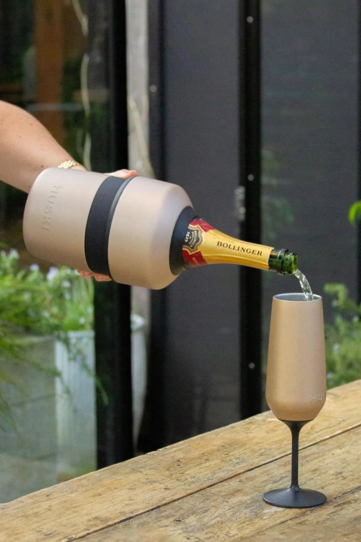 Bottle of Bollinger champagne being poured into a glass on a wooden surface with a blurred background.