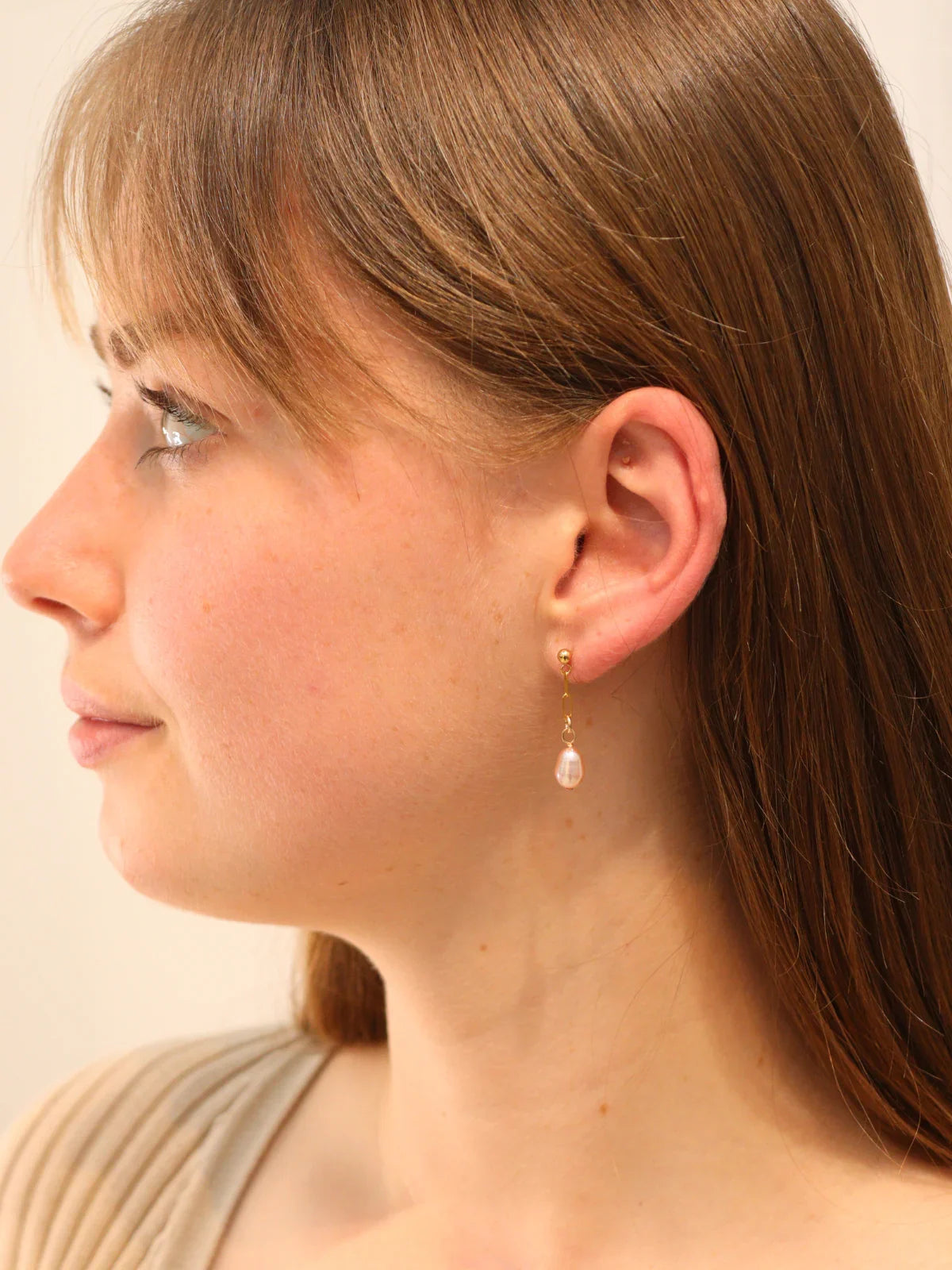 Woman wearing delicate gold drop earrings with teardrop pearl charms.