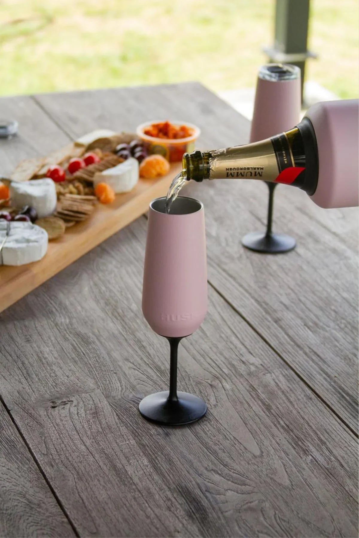 Pink wine glass being filled with a bottle on a wooden table outdoors.