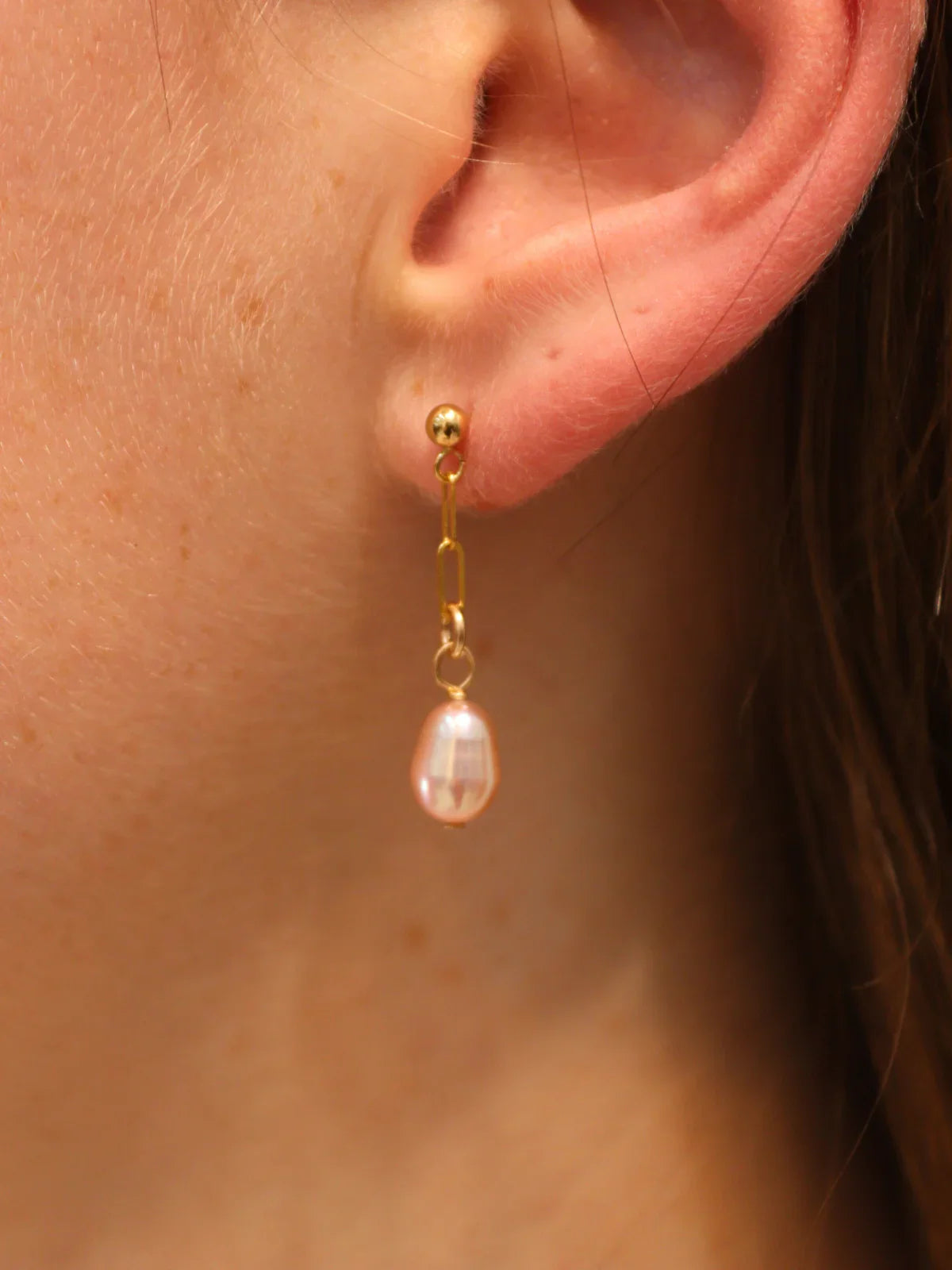 Close-up of gold chain link drop earring with single teardrop pearl.