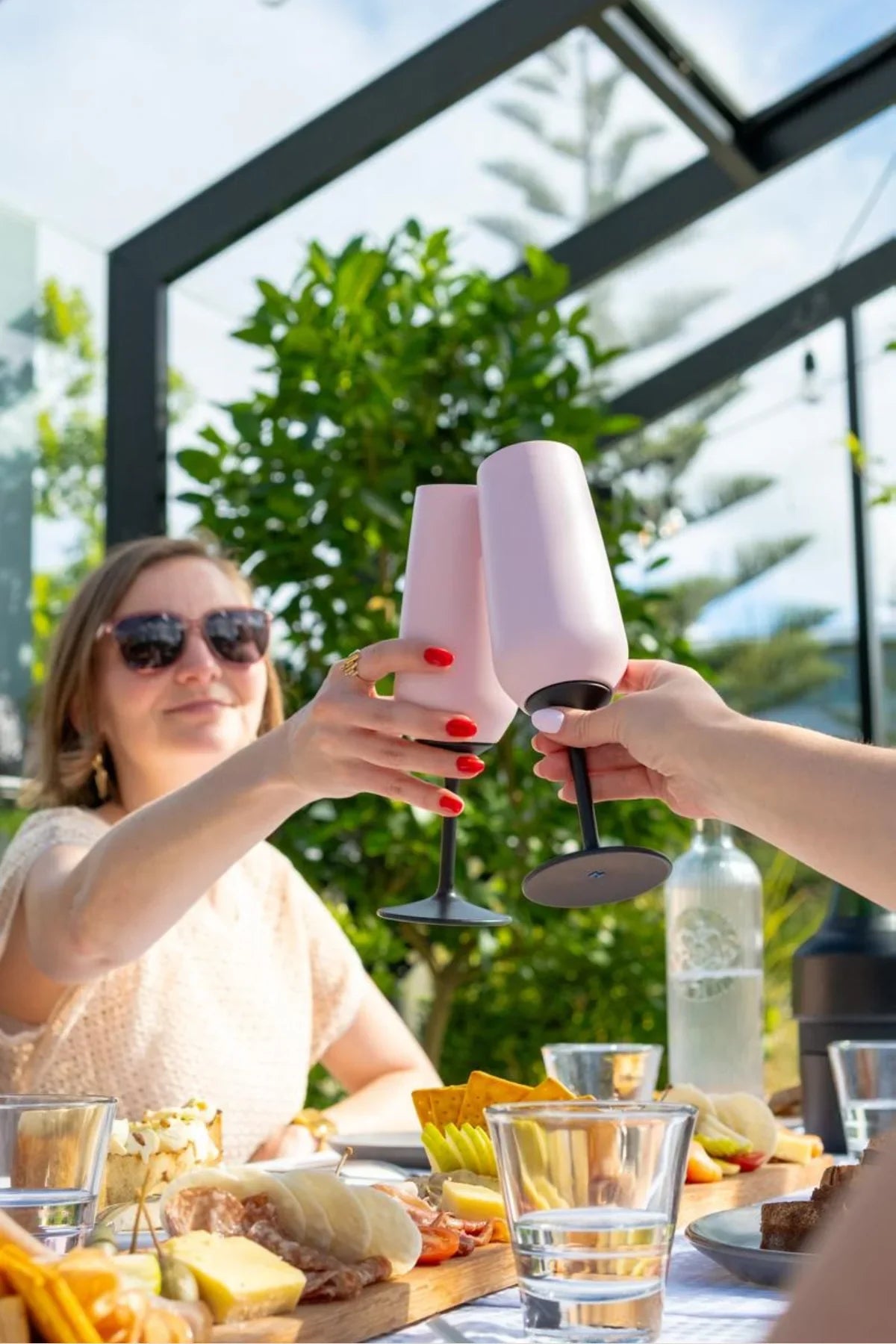 Two people clinking pink wine glasses outdoors with a scenic background