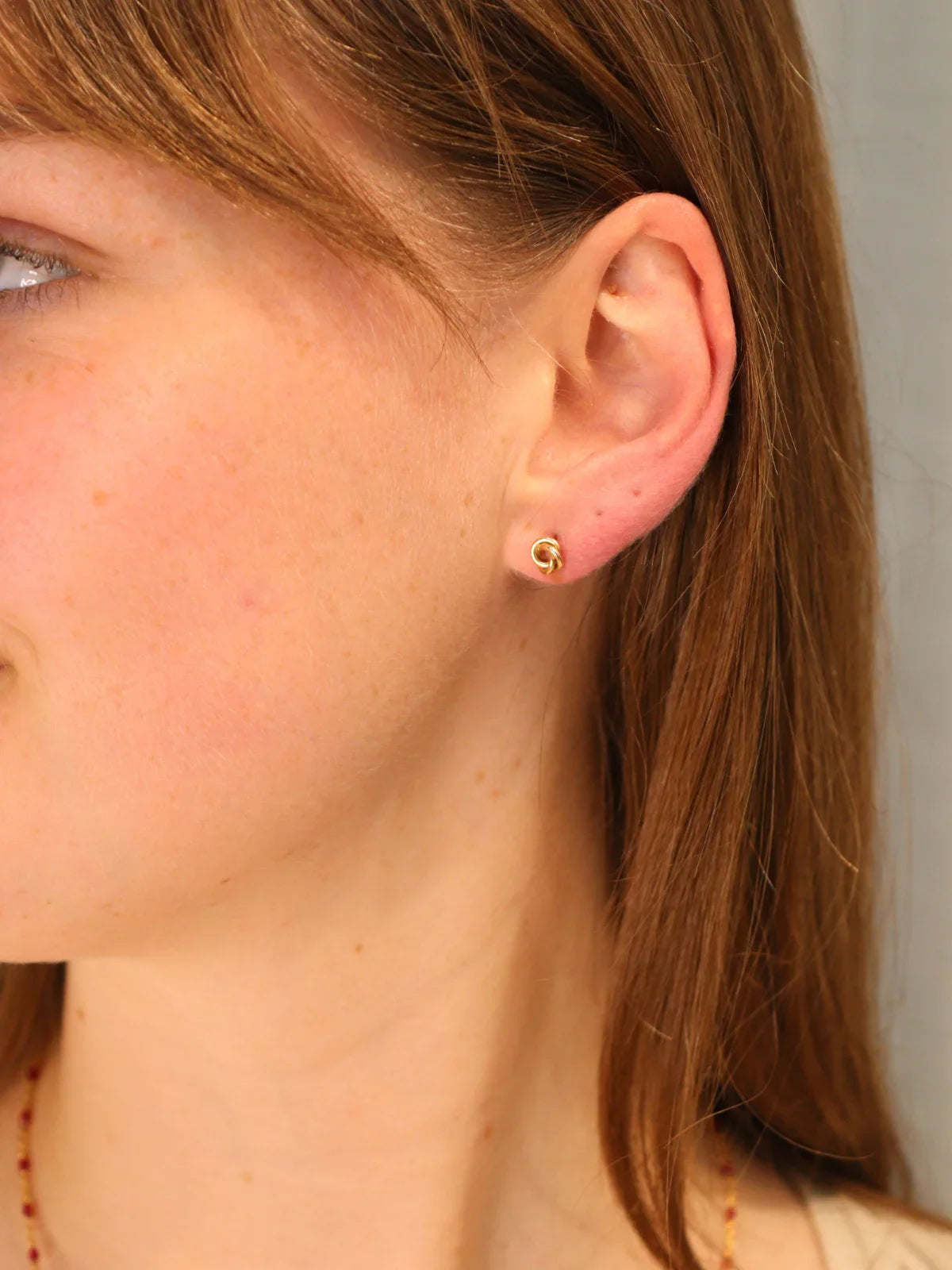 Simple gold knot stud earring, shown on ear.