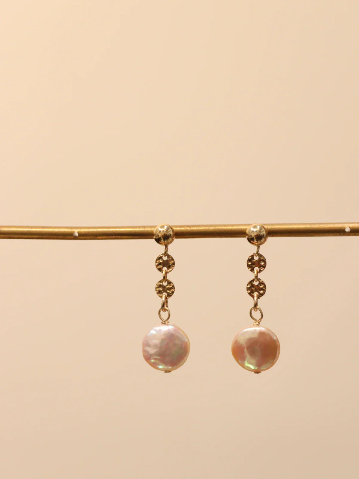 Pair of gold drop earrings with white pearls, displayed on jewelry stand.
