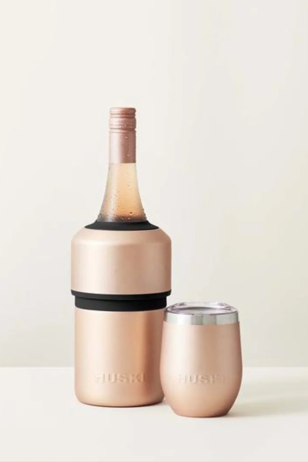 Rose gold wine bottle and matching glass on a light background
