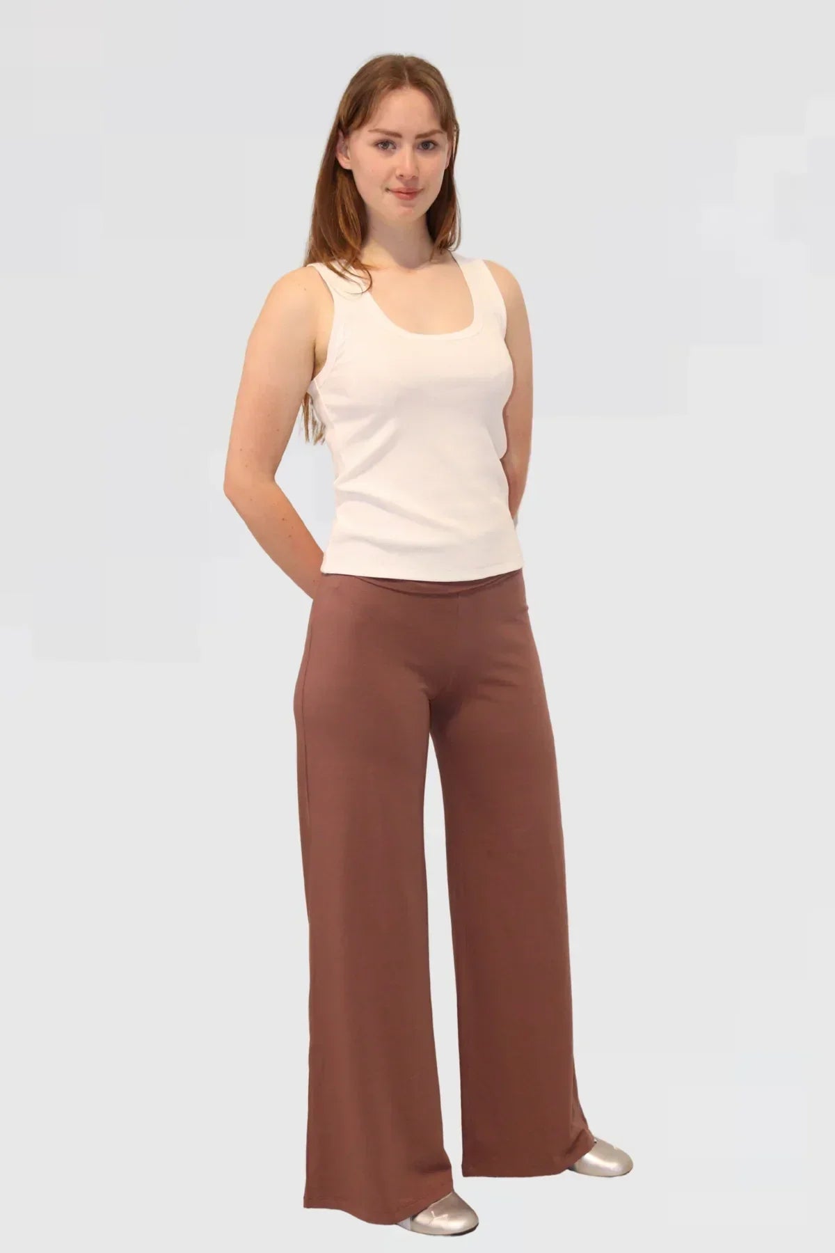 Woman wearing a white tank top and brown yoga pants a light grey background