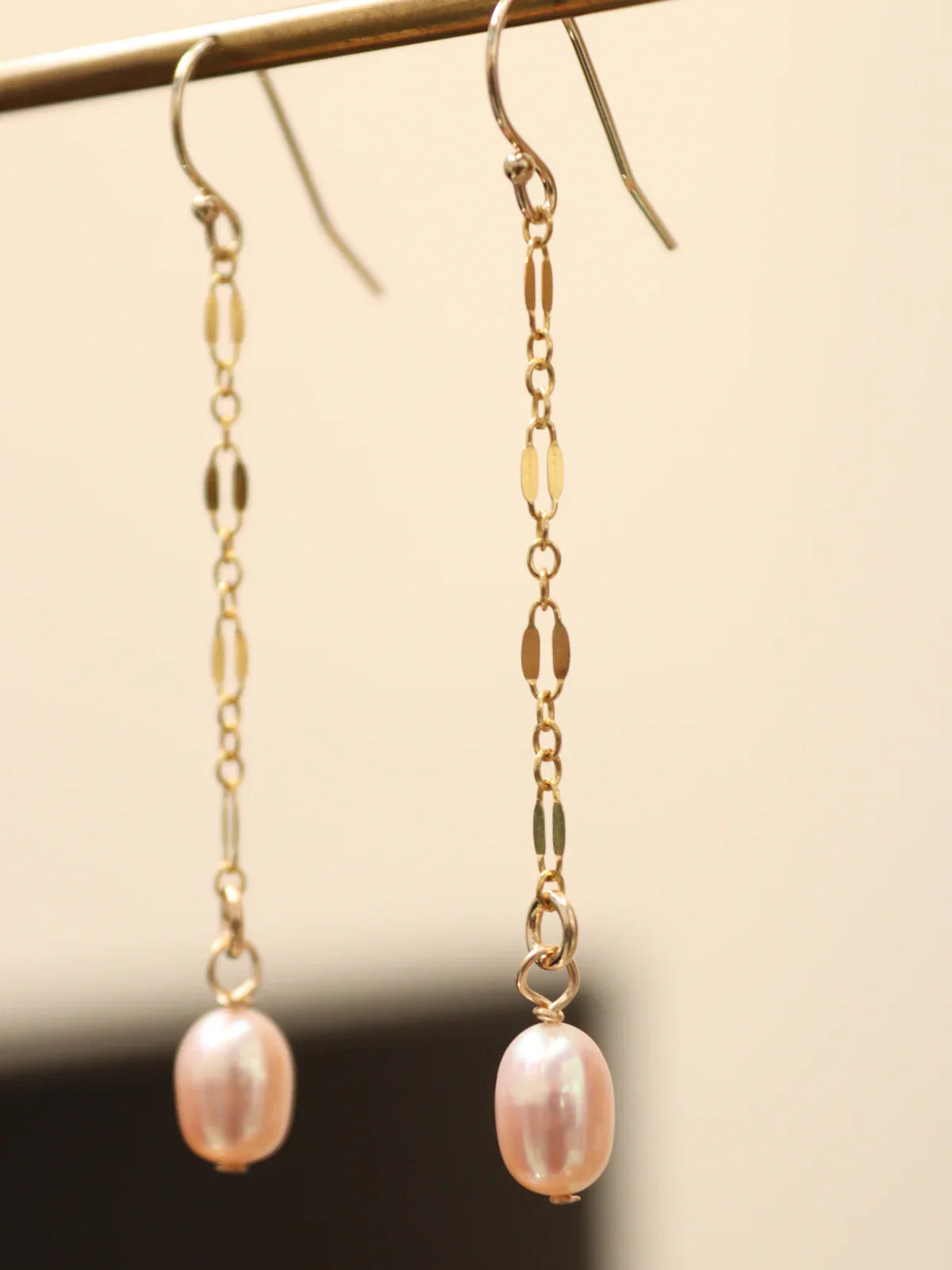 Gold chain earrings with pink pearls on a neutral background