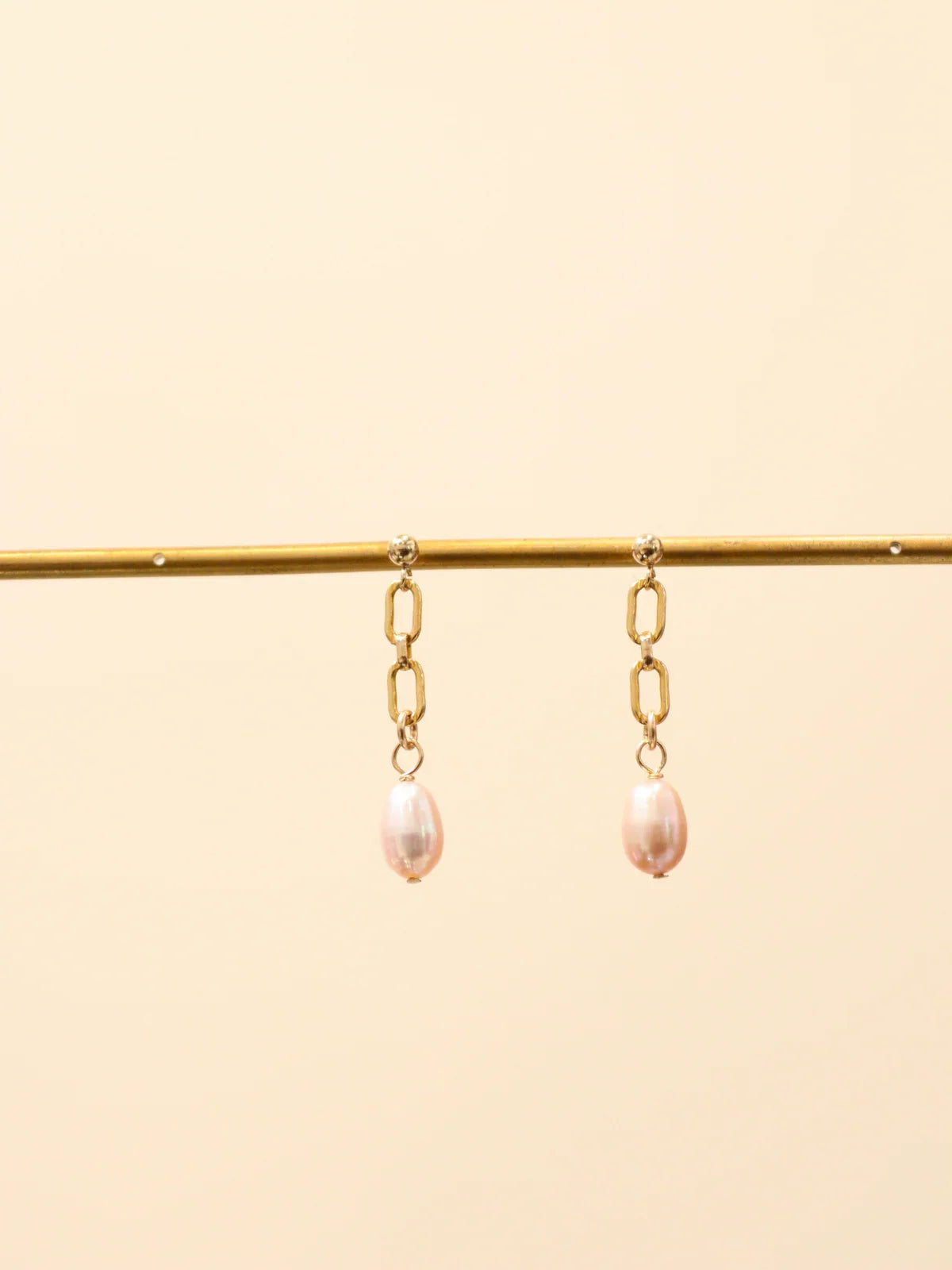 Pair of gold chain link drop earrings with oval white pearls, displayed on a jewellery stand